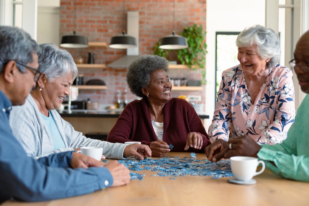 A group of older adults working on a jigsaw puzzle together at a kitchen table